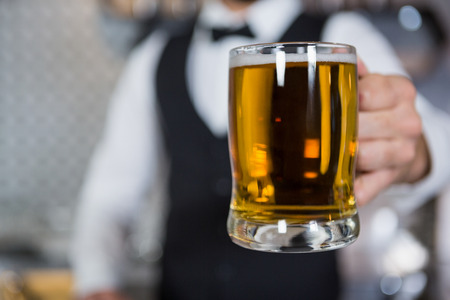 Mid section of bartender holding glass of beer in bar counter at barの写真素材