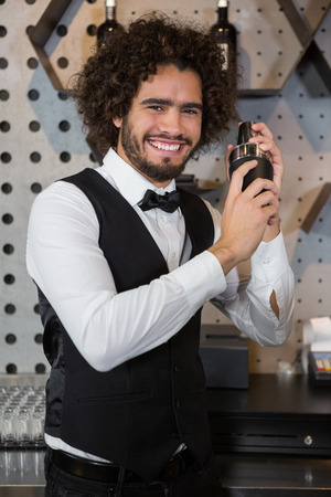 Portrait of happy waiter shaking drink in cocktail shaker in a barの写真素材