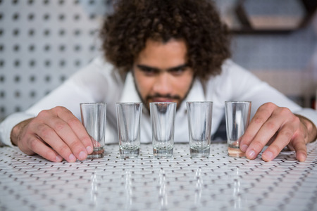 Bartender placing shot glasses in a row on bar counter in barの写真素材