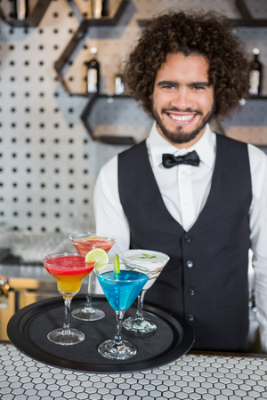 Portrait of bartender holding tray of cocktails and milkshake in barの写真素材