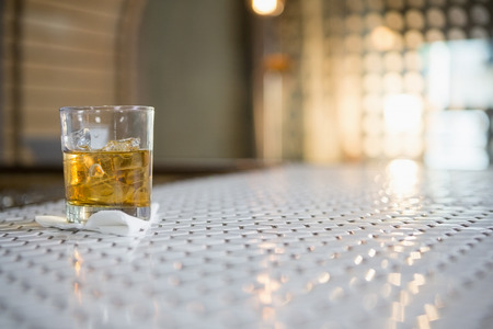 Glass of whisky with ice cube on bar counter at barの写真素材