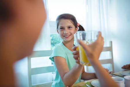 Smiling girl toasting her juice glass at breakfast table