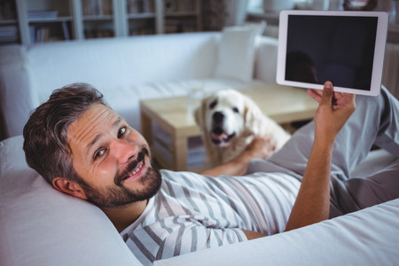 Portrait of smiling, man holding digital tablet in living roomの写真素材