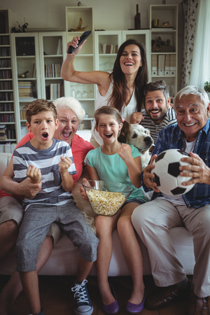 Happy multi-generation family watching soccer match on television in living room at homeの写真素材