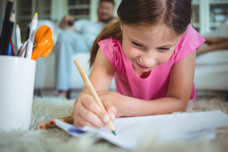 Smiling girl lying on the floor and drawing while parents sitting on sofaの写真素材