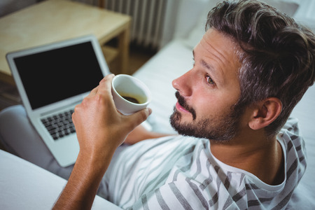 Father using laptop while having coffee in living room at homeの写真素材
