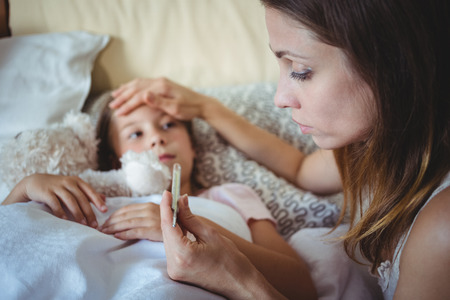 Mother checking daughters temperature on thermometer at homeの写真素材