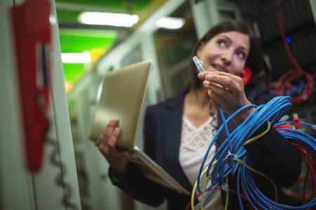 Technician holding internet cable while talking on phone in server room