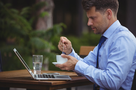 Handsome businessman having tea while using laptop at outdoor cafÃ©の写真素材