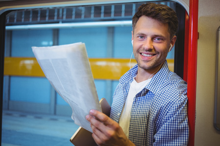 Portrait of handsome man holding newspaper while listening music in trainの写真素材