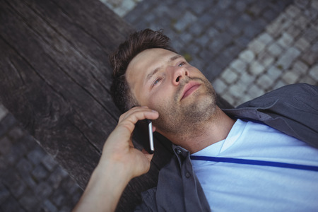 Handsome business executive lying on wood while talking on mobile phone