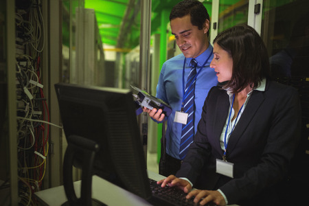 Technicians using digital cable analyzer while working on personal computer in server room