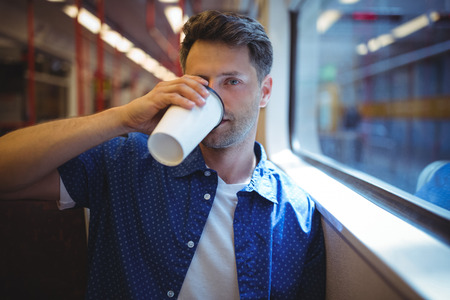 Handsome man drinking coffee in trainの写真素材