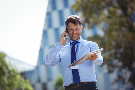 Portrait of handsome businessman holding laptop while talking on mobile phoneの写真素材