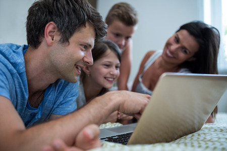 Happy family using laptop in bedroom at home
