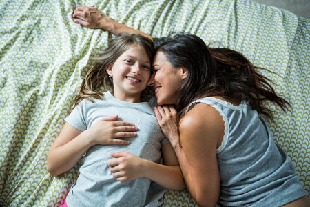Mother and daughter playing on bed at homeの写真素材