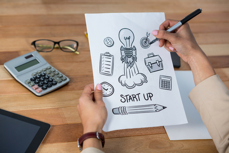 Businesswoman drawing icons on paper in officeの写真素材