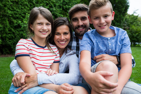 Portrait of happy family sitting on grass in park on a sunny day