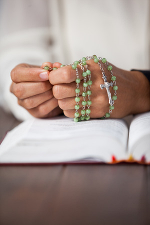 Praying hands of woman with a rosary and bible on wooden deskの写真素材