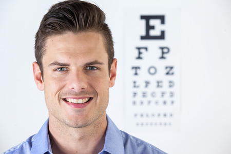 Portrait of man wearing contact lens with eye chart in backgroundの写真素材