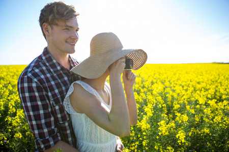 Couple taking picture from camera in mustard field on a sunny day