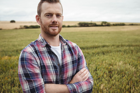 Portrait of farmer standing with arms crossed in the field on a sunny dayの写真素材