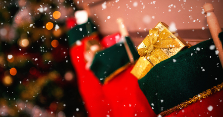 Snow falling against christmas stockings hanging on fireplace with gifts