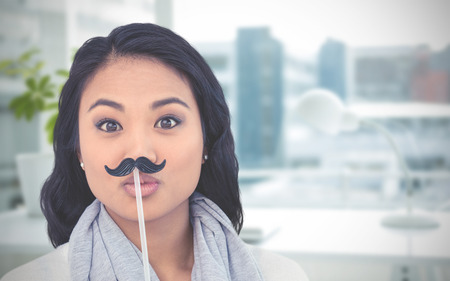 Pretty Asian woman with fake mustache posing for camera against documents are posing on the desk