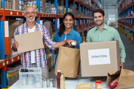 Three volunteers packing eatables in cardboard box in a warehouse