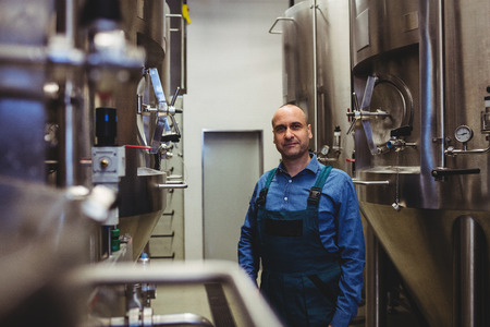 Portrait of confident owner standing amidst manufacturing equipment at brewweryの写真素材