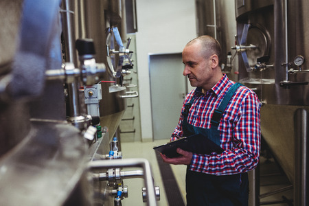 Side view of manufacturer examining machinery at brewery