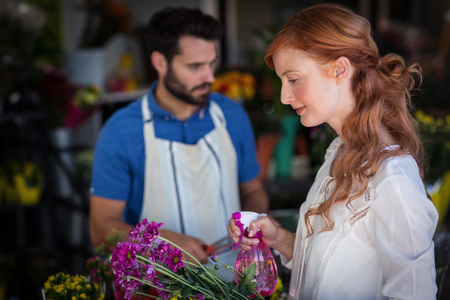 Woman spraying water on bunch of flowers while man preparing flower bouquet in the flower shopの写真素材