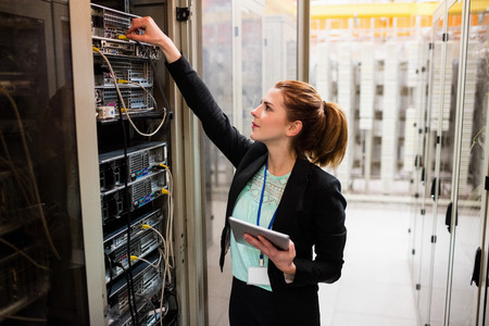 Technician holding digital tablet while examining server in server room