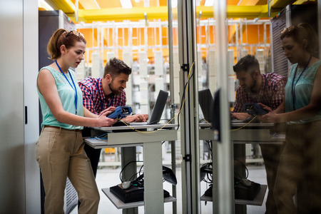 Technicians using laptop while analyzing server in server room