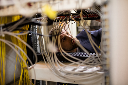 Technician checking cables in a rack mounted server in server room