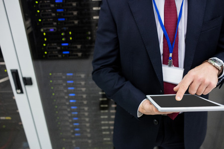 Mid section of technician using digital tablet in server room