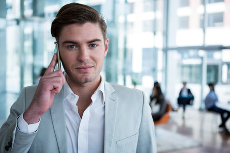 Portrait of businessman talking on mobile phone in the officeの写真素材