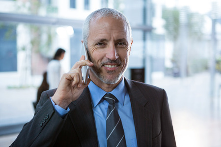 Portrait of businessman talking on mobile phone in officeの写真素材