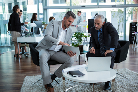 Businesspeople discussing over digital tablet in officeの写真素材