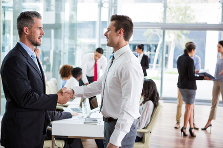 Businessmen interacting with each other while shaking hands in officeの写真素材