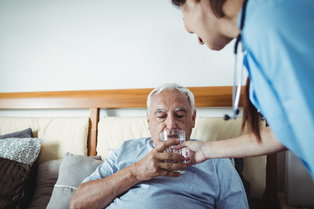 Nurse giving a glass of water to senior man at homeの写真素材