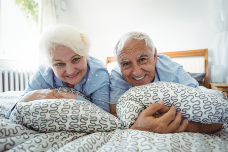 Portrait of senior couple smiling on bed at bedroomの写真素材