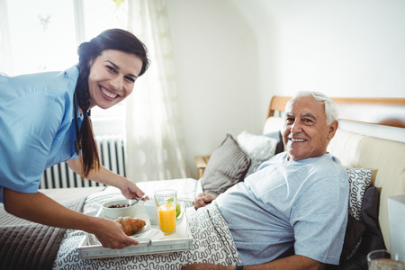 Nurse serving breakfast to senior man at homeの写真素材