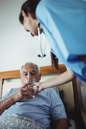 Nurse giving a glass of water to senior man at homeの写真素材