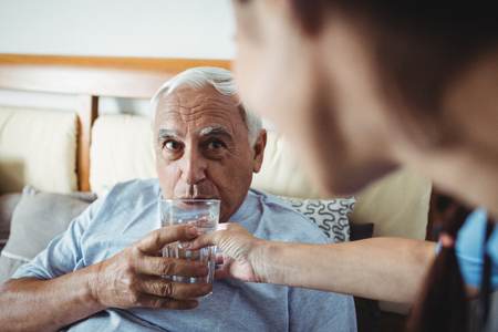 Nurse giving a glass of water to senior man at homeの写真素材