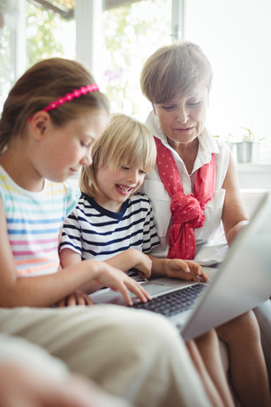 Grandchildren using laptop with their grandmother at home