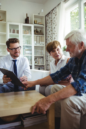 Senior couple planning their investments with financial advisor in living roomの写真素材