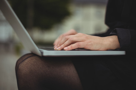 Mid section of businesswoman using laptop in office campusの写真素材
