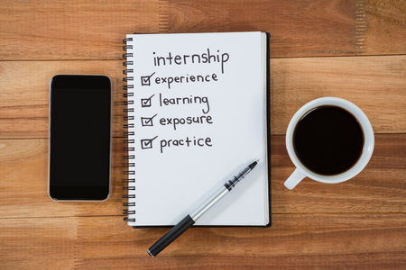 Close-up of coffee cup with mobile phone and belongings on table in officeの写真素材