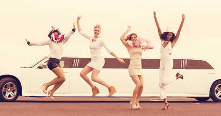 Happy friends jumping in front of a limousine on night outの写真素材